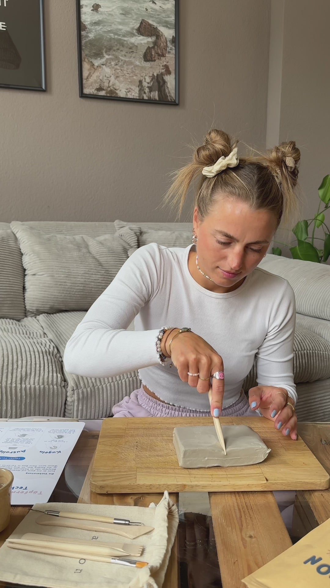 Frau töpfert mit dem Töpferset das erste Mal zuhause auf ihrem Couchtisch mit Lufttrocknendem Ton und Modellierhölzern